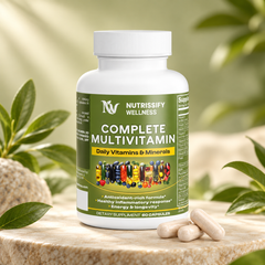A white bottle of NutriSify Wellness Complete Multivitamin with a green label, displayed on a stone pedestal with three beige capsules in front, surrounded by soft-focus green leaves.